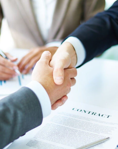 Image of business partners handshaking over business objects on workplace